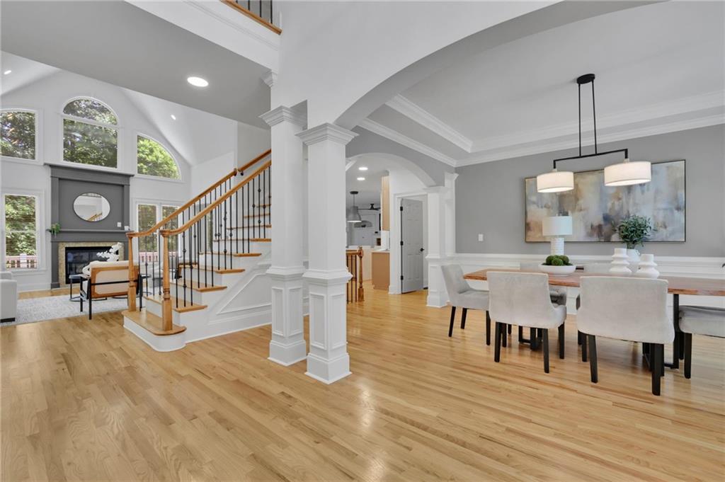 Open living and dining area with a fireplace, arched windows, and a wood-railed staircase.