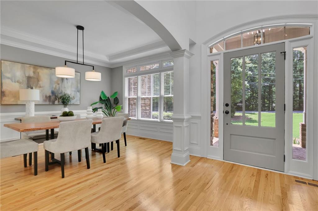 Dining area with a wood table and upholstered chairs beside a gray glass-paneled front door.