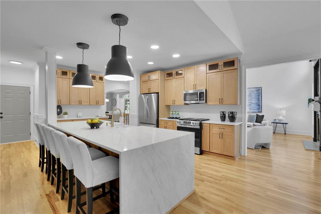 Open-plan kitchen with a large white island, light wood cabinets, and stainless steel appliances.