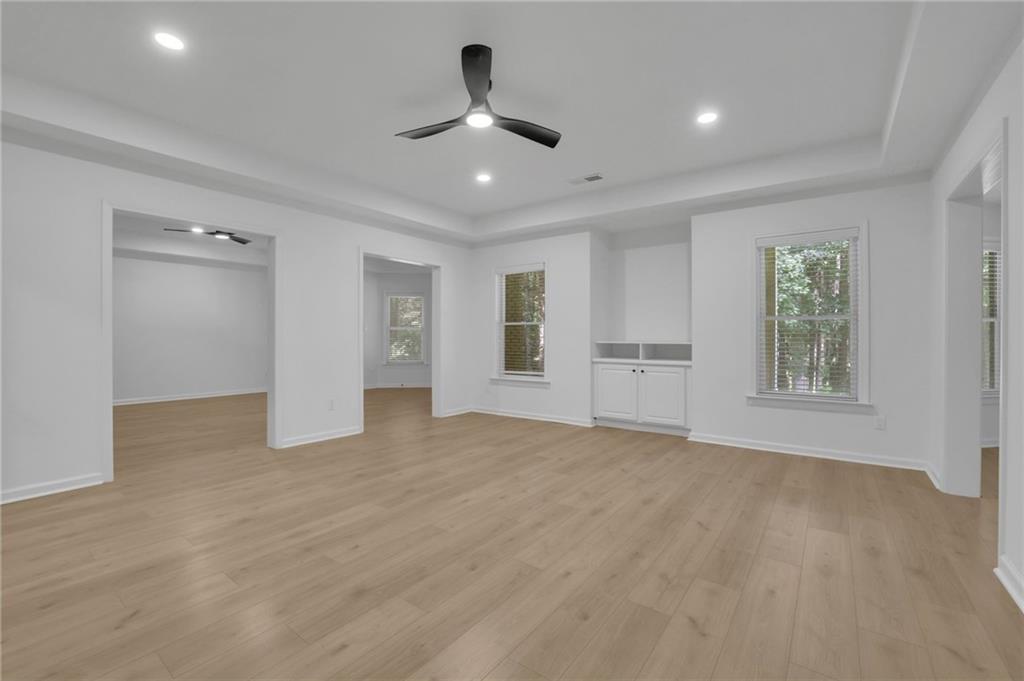 Unfurnished living area with light wood floors, a tray ceiling, and built-in cabinets beneath the windows.