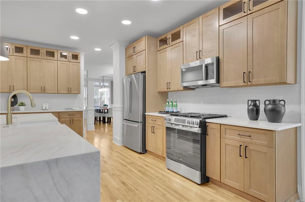 Kitchen with light wood cabinets, a marble island, stainless steel appliances, and hardwood floors.