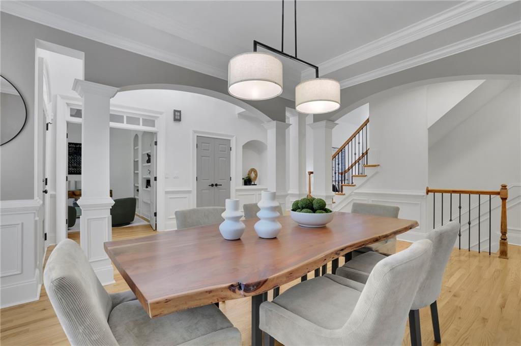 Dining room with a natural-edge wood table, gray chairs, white columns, and a staircase.