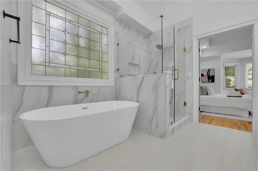 Bathroom with a freestanding tub, glass shower, brass fixtures, and a decorative stained-glass window.