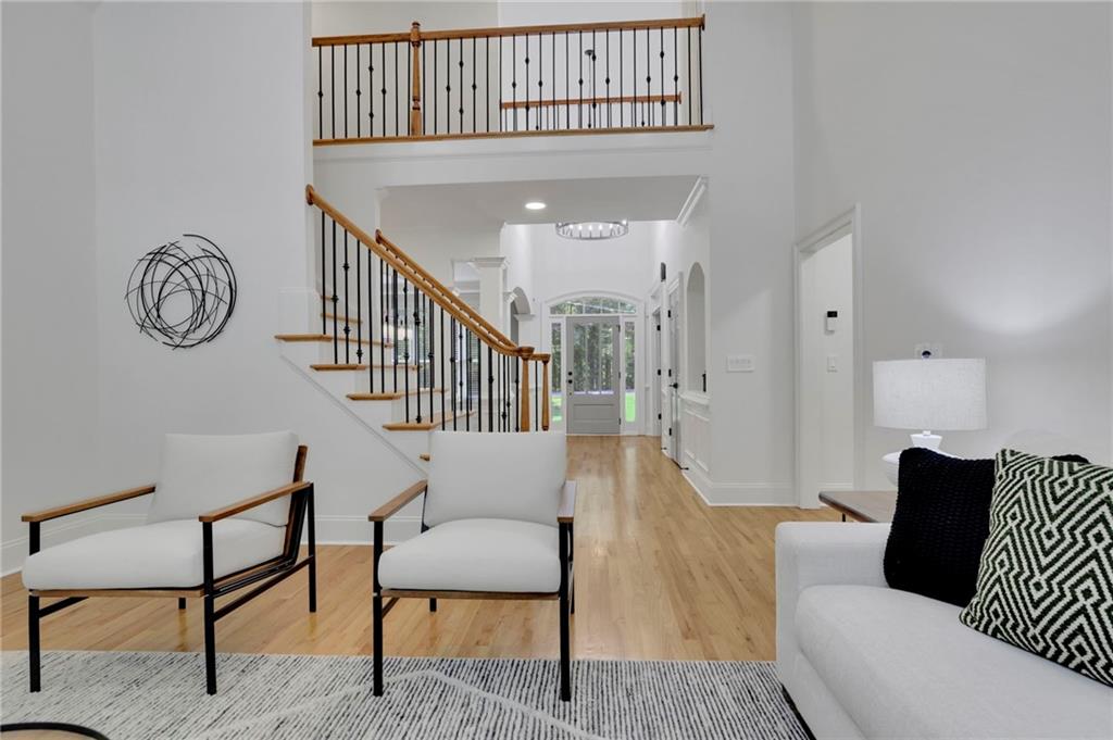 Living room with white seating, light wood floors, and a staircase overlooking the entryway.