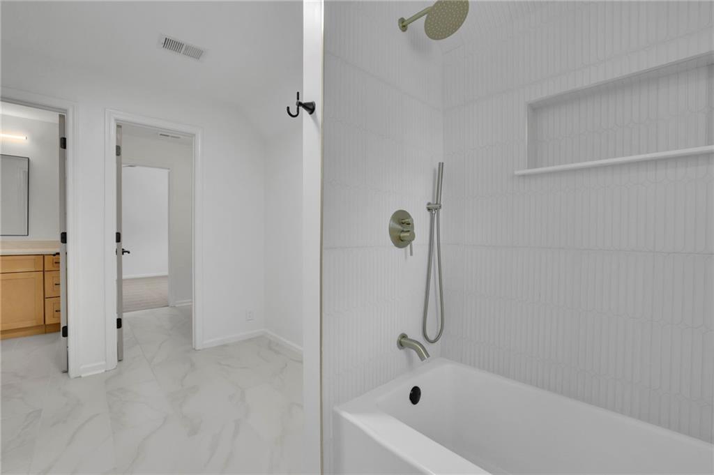Bathroom with a white tub, tiled shower niche, marble-look flooring, and a glimpse of a wood vanity.