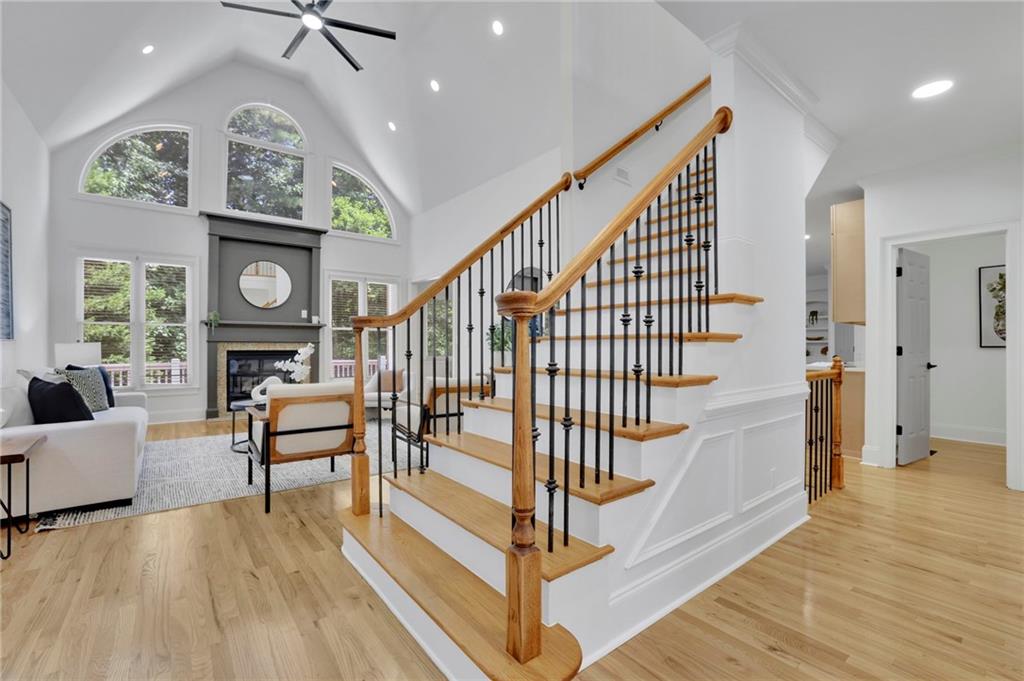 Living room with a fireplace, arched windows, vaulted ceiling, and prominent wood-and-black-metal staircase.