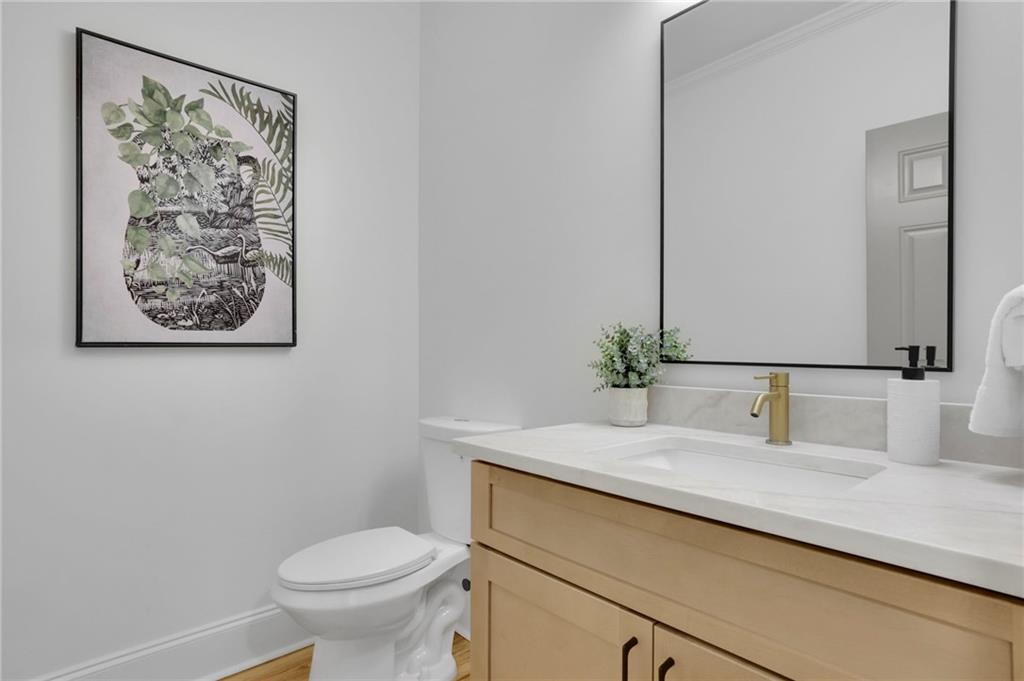 Bathroom with a light wood vanity, brass faucet, large mirror, and framed botanical artwork.