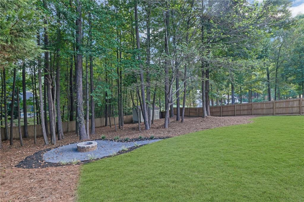 Backyard with a green lawn, wooded fence line, and a small fire pit.