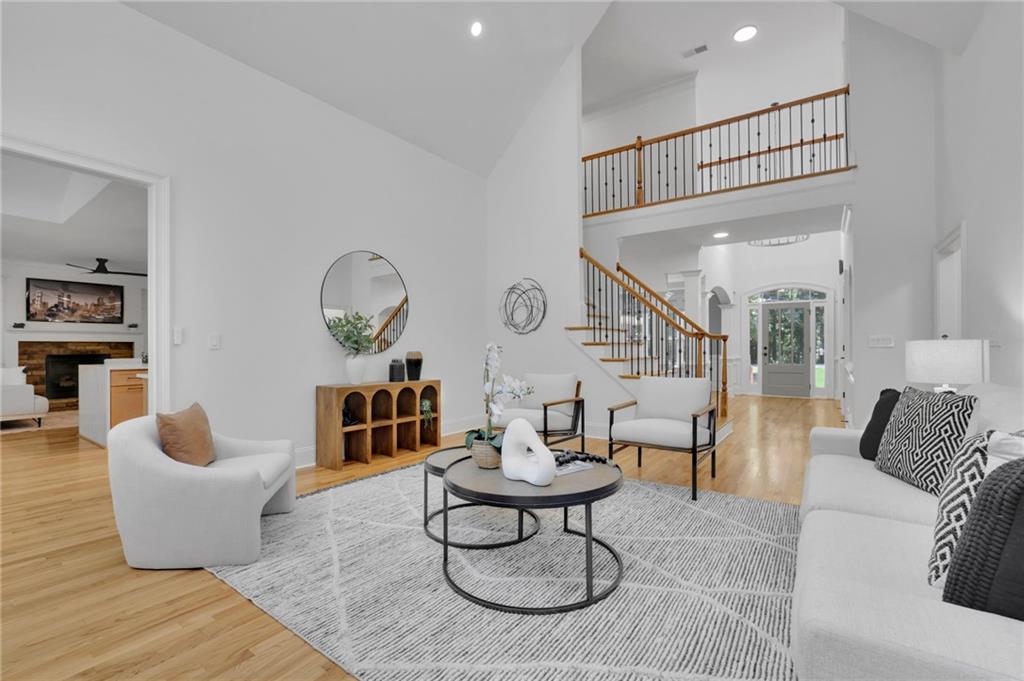 Staged living room with vaulted ceiling, white sofas, and an open staircase overlooking the foyer.