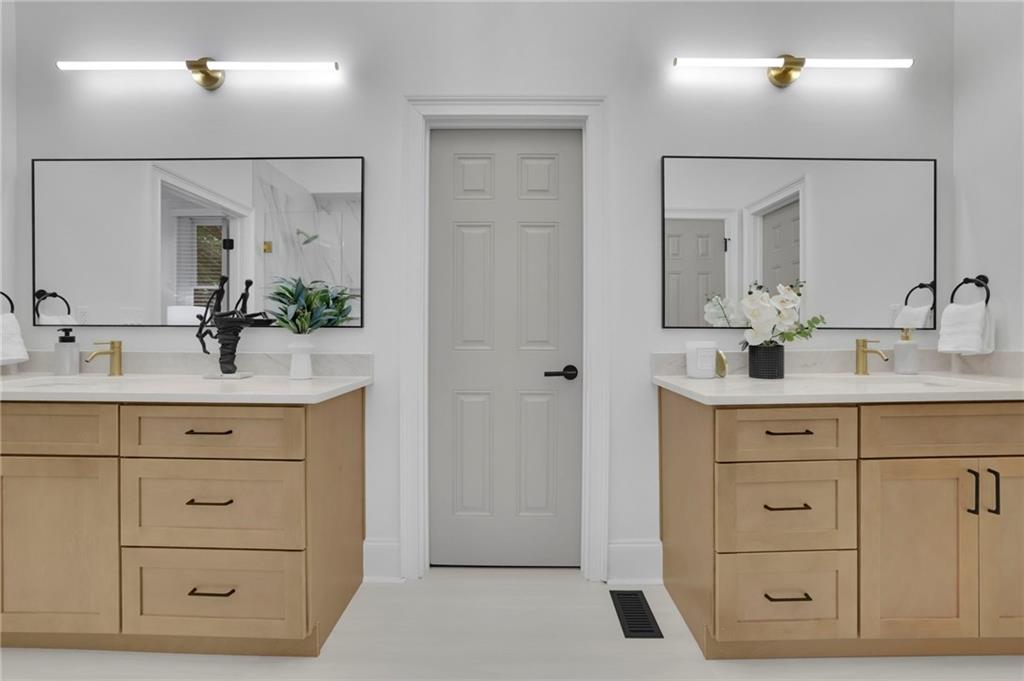 Bathroom with matching double vanities, light wood cabinets, and large mirrors.
