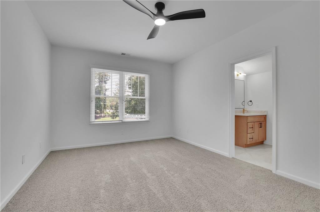 Empty carpeted bedroom with a ceiling fan, window, and doorway to an ensuite bathroom.