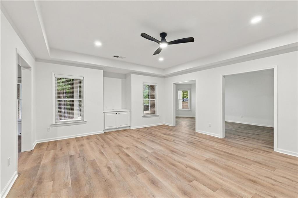 Empty room with light wood floors, a tray ceiling, and a black ceiling fan.