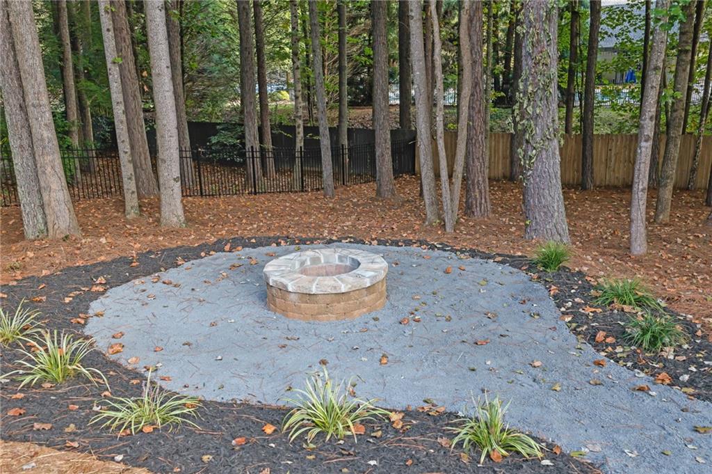 Stone fire pit on a gravel patio in a wooded, fenced backyard.