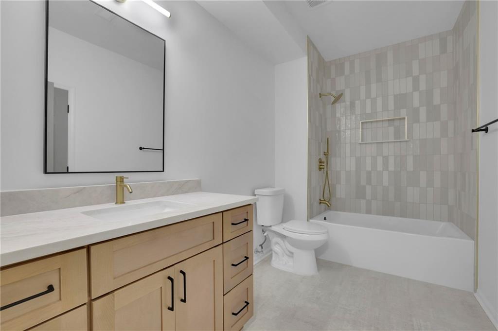 Bathroom with a light wood vanity and tiled tub-shower with brass fixtures.