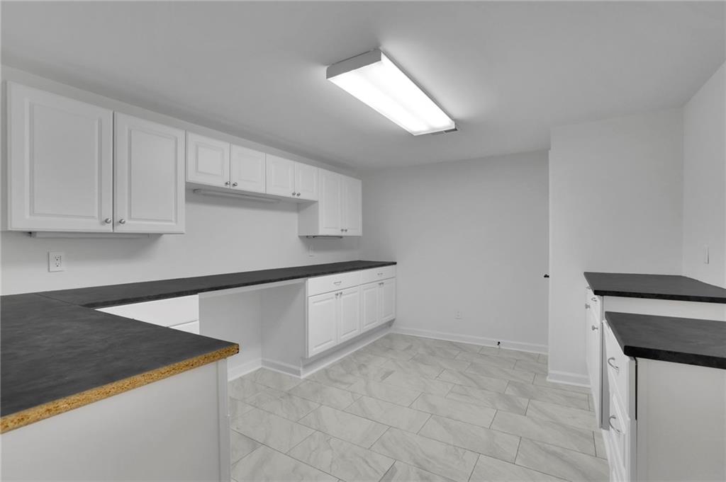 Empty kitchen with white cabinets, dark countertops, and light tile flooring.