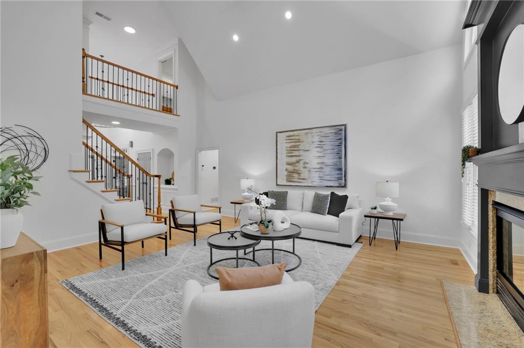 Staged living room with a vaulted ceiling, hardwood floors, a two-story staircase, and a fireplace.