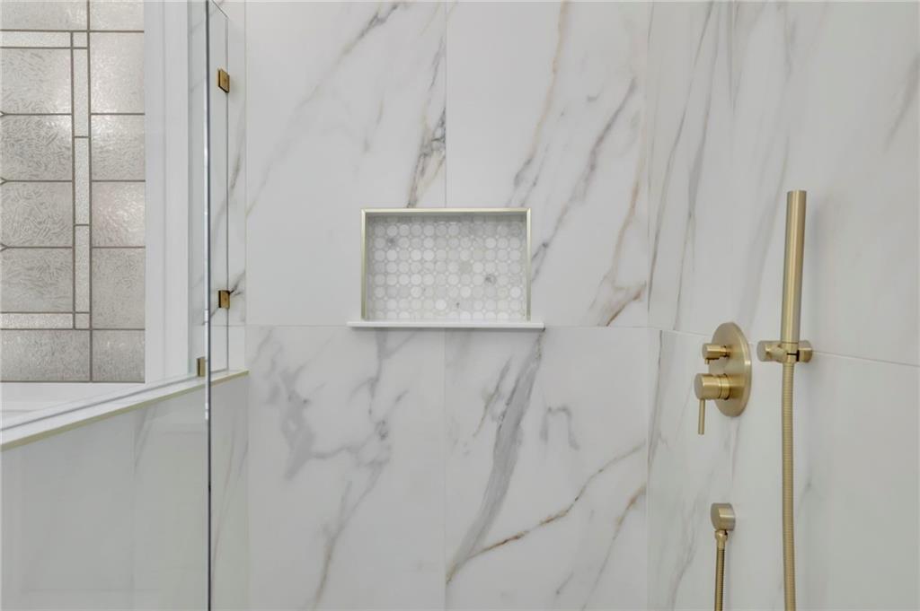 Marble-tiled shower with a glass enclosure, recessed mosaic niche, and brass fixtures.