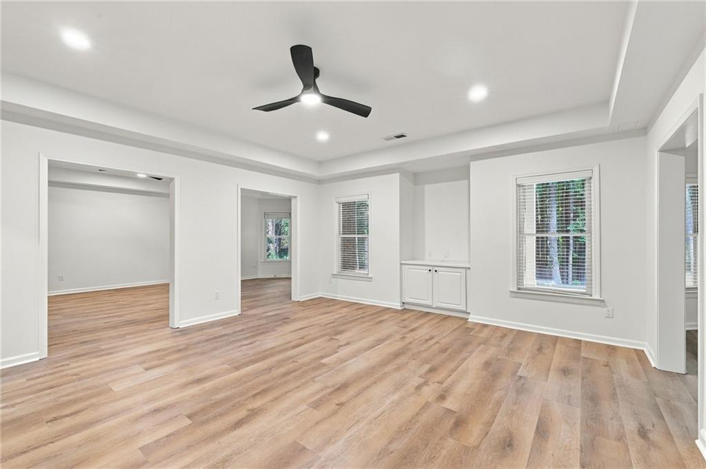 Empty room with wood-look floors, a tray ceiling, and a built-in cabinet between windows.