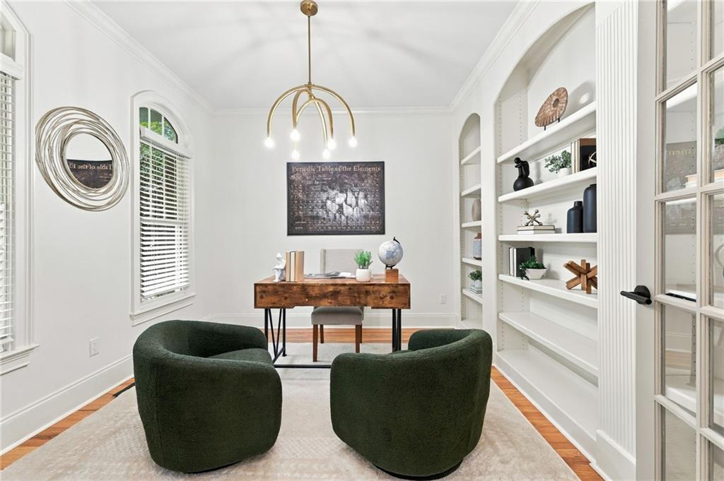 Bright home office with white built-in shelves, wooden desk, and two dark green chairs.