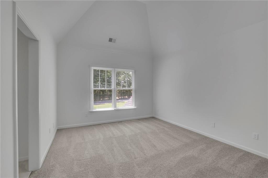Empty bedroom with light carpet, a high ceiling, and a double window overlooking trees and lawn.