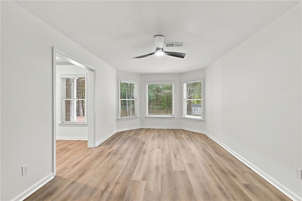 Vacant room with wood-look floors, a ceiling fan, and three bay windows.