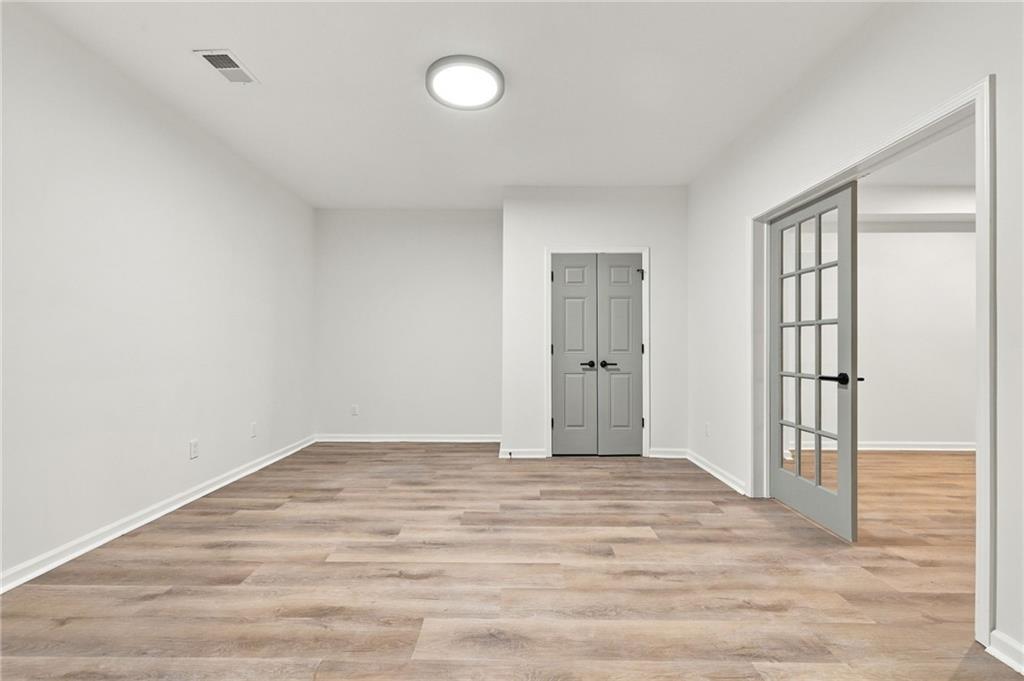 Empty room with wood-look flooring, gray double doors, and an open glass-paneled doorway.