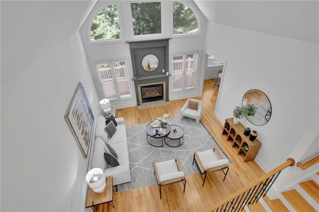 Staged double-height living room with a gray fireplace, arched windows, and hardwood floors.