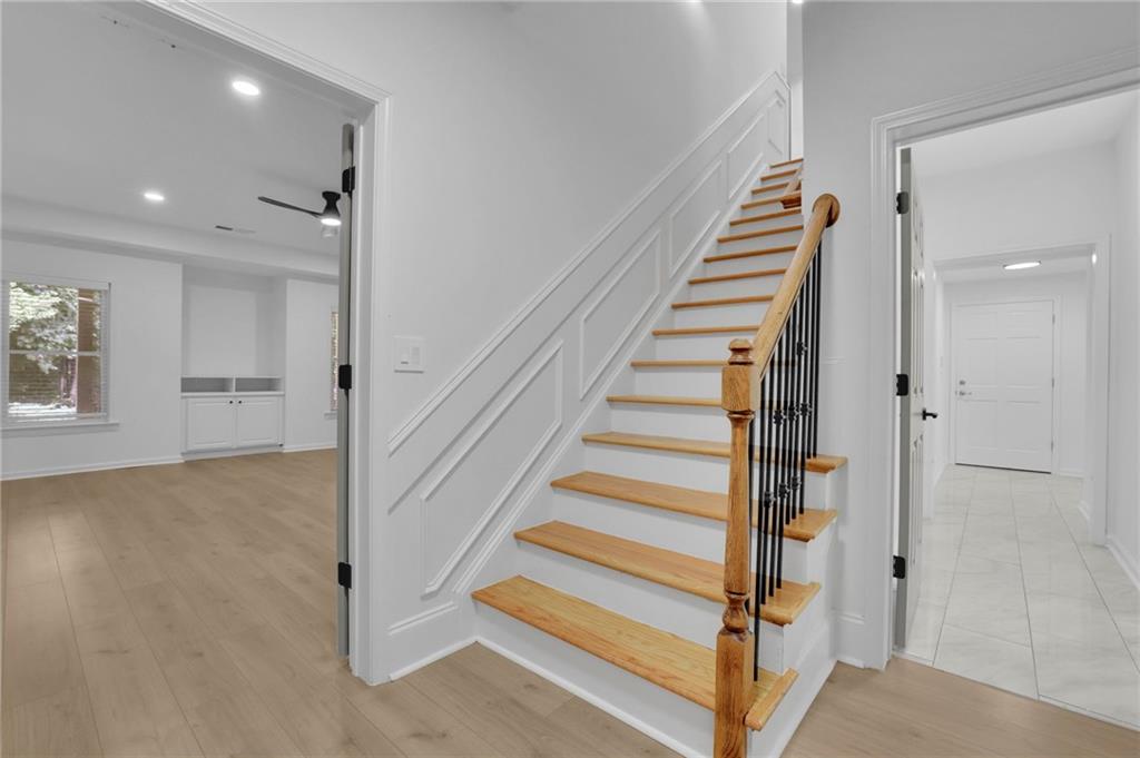 Interior staircase with wood treads and black balusters, between an open room and tiled hallway.