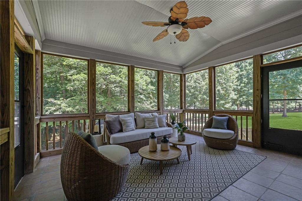 Screened porch with wicker seating, patterned rug, and views of leafy trees.