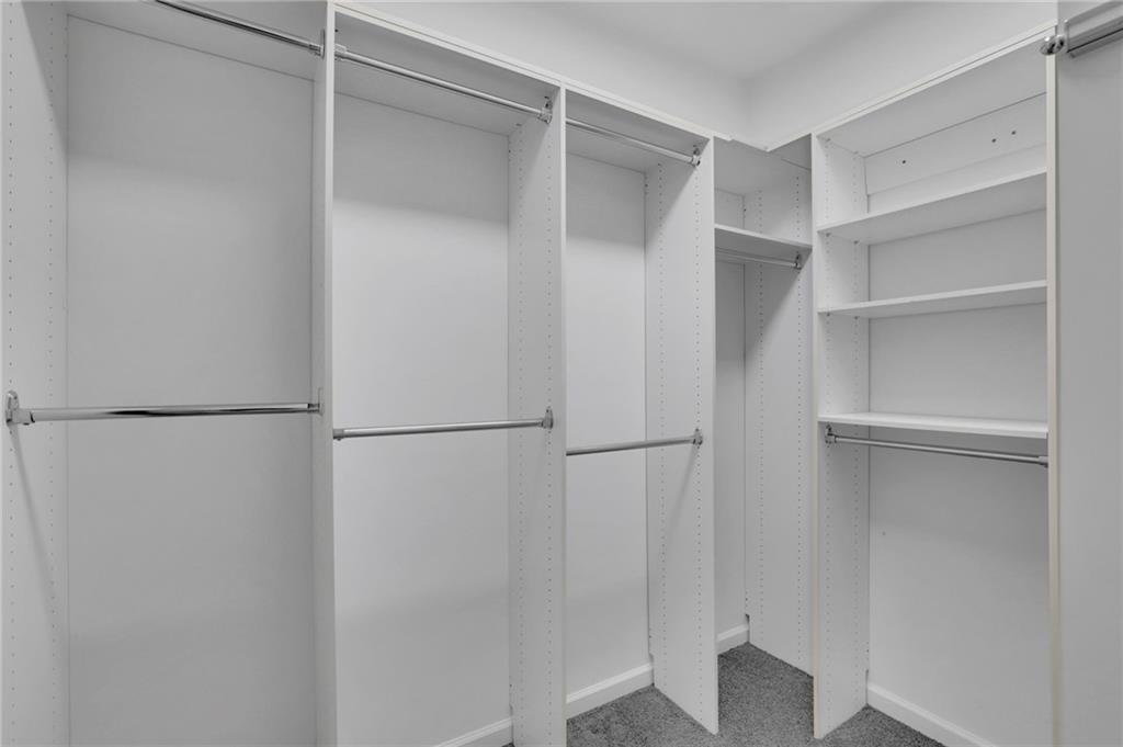 Walk-in closet with white built-in shelving, multiple hanging rods, and gray carpet.