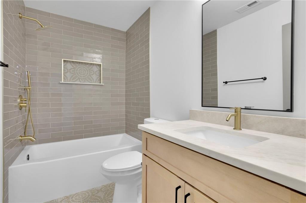 Bathroom with tiled tub and shower, light wood vanity, brass fixtures, and a large framed mirror.