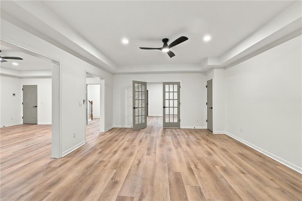 Empty room with wood-look floors, a tray ceiling, and glass-paneled French doors.