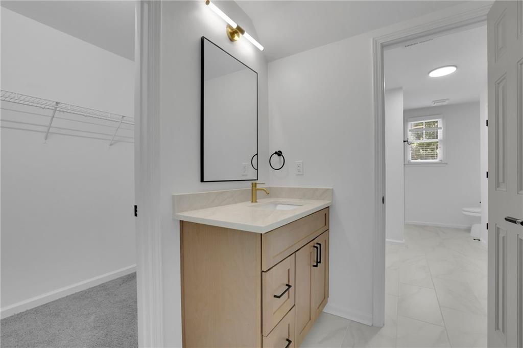 Bathroom vanity with a gold faucet and black-framed mirror beside an open closet and tiled bathroom.