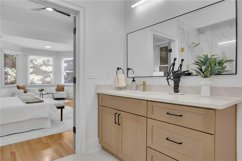Bathroom vanity with light wood cabinetry and large mirror, opening onto a bright bedroom.