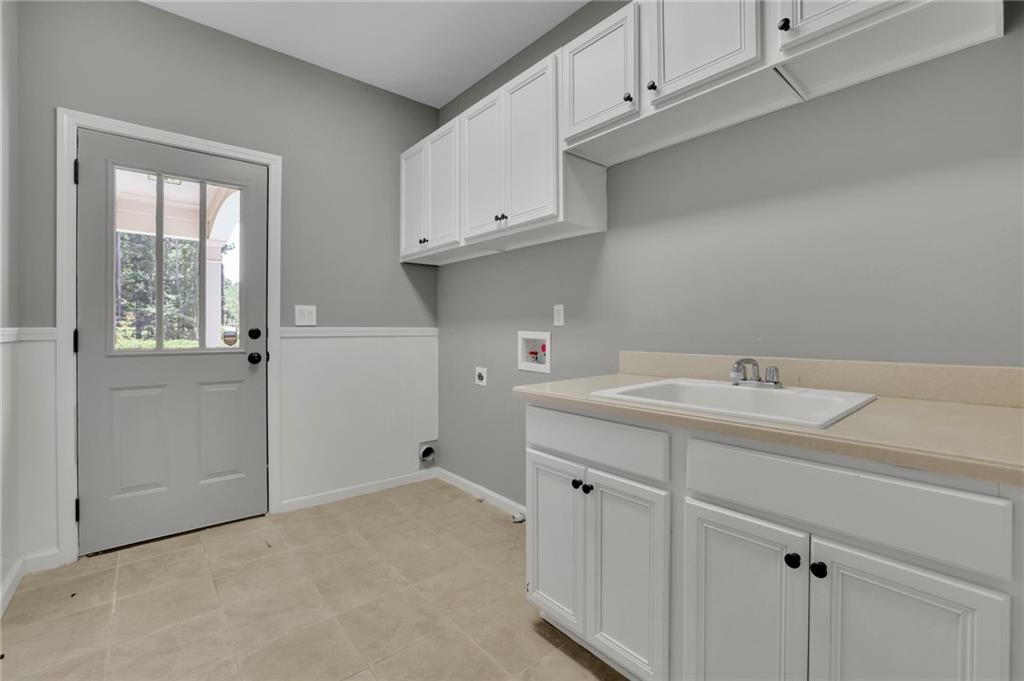 Laundry room with a utility sink, white cabinets and a windowed exterior door.