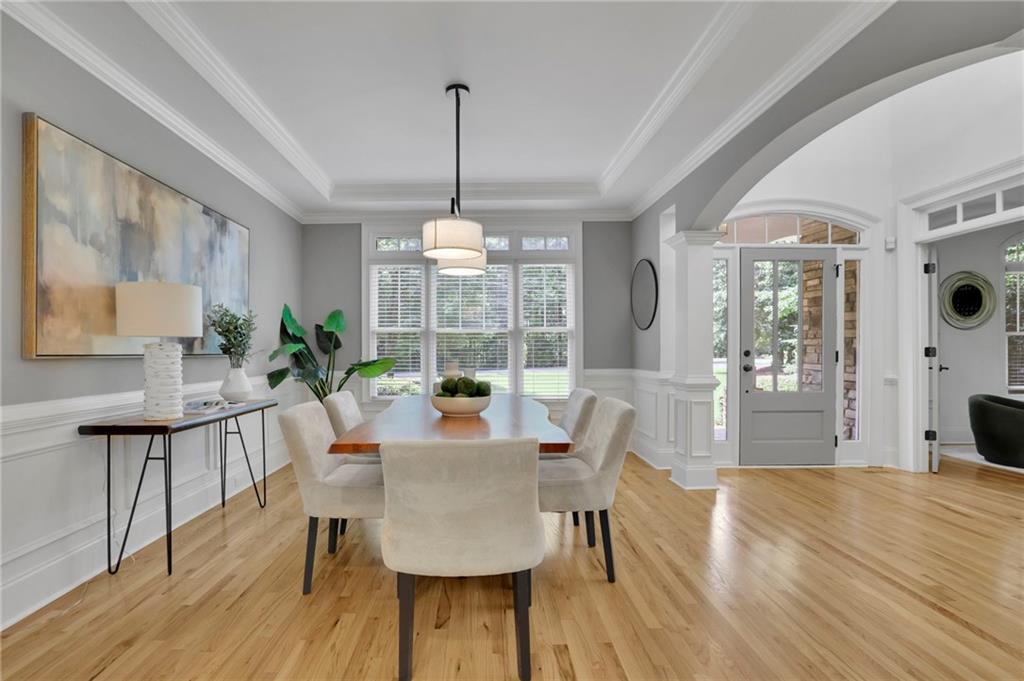 Dining room with a wood table, upholstered chairs, hardwood floors, and an arched entryway.