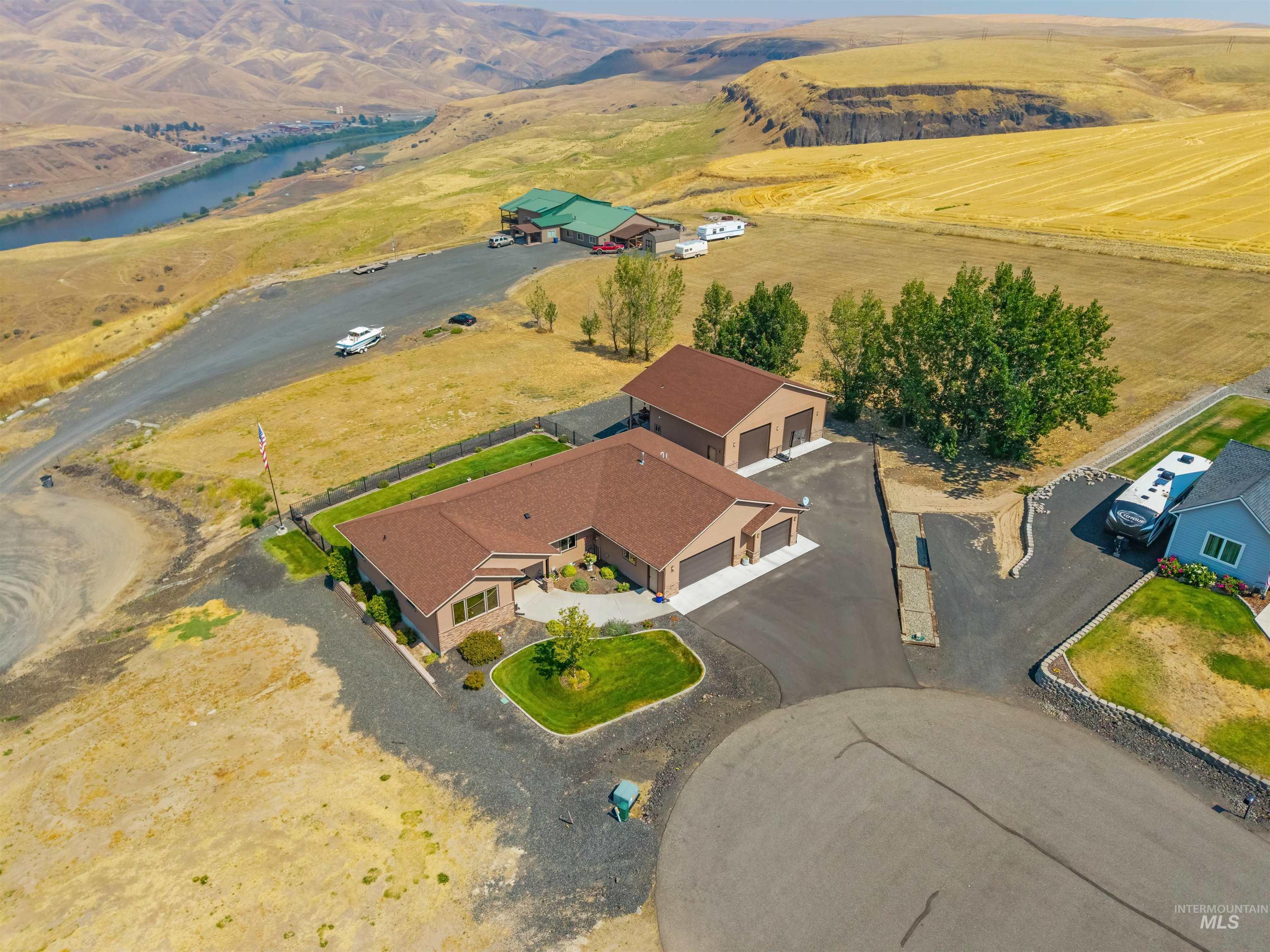 Aerial view of a rural home with a fenced lawn, detached outbuilding, and river beyond.