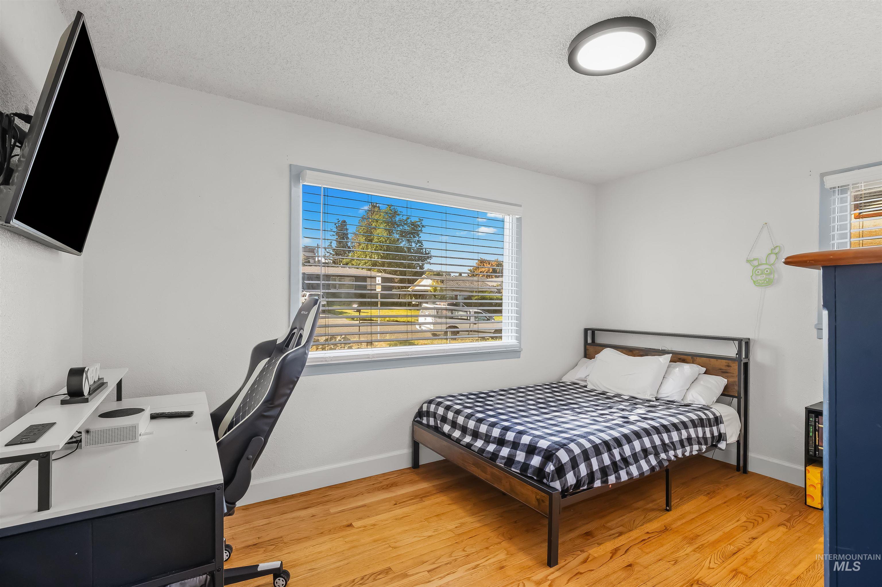 Bedroom with a checkered bed, gaming desk and chair, and warm hardwood floors.
