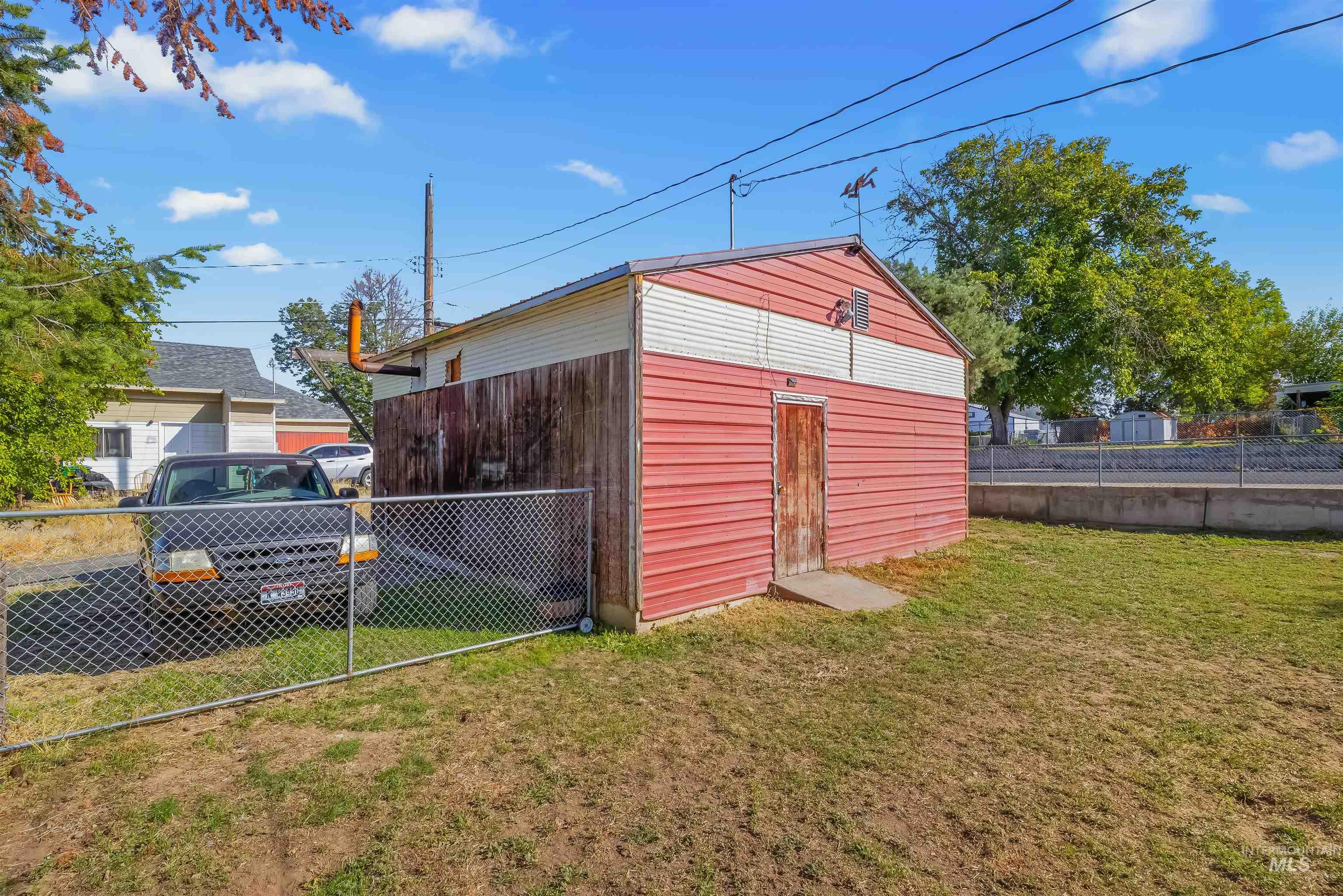 Red detached garage with white siding accents, a weathered wooden door, and a chain-link fence.