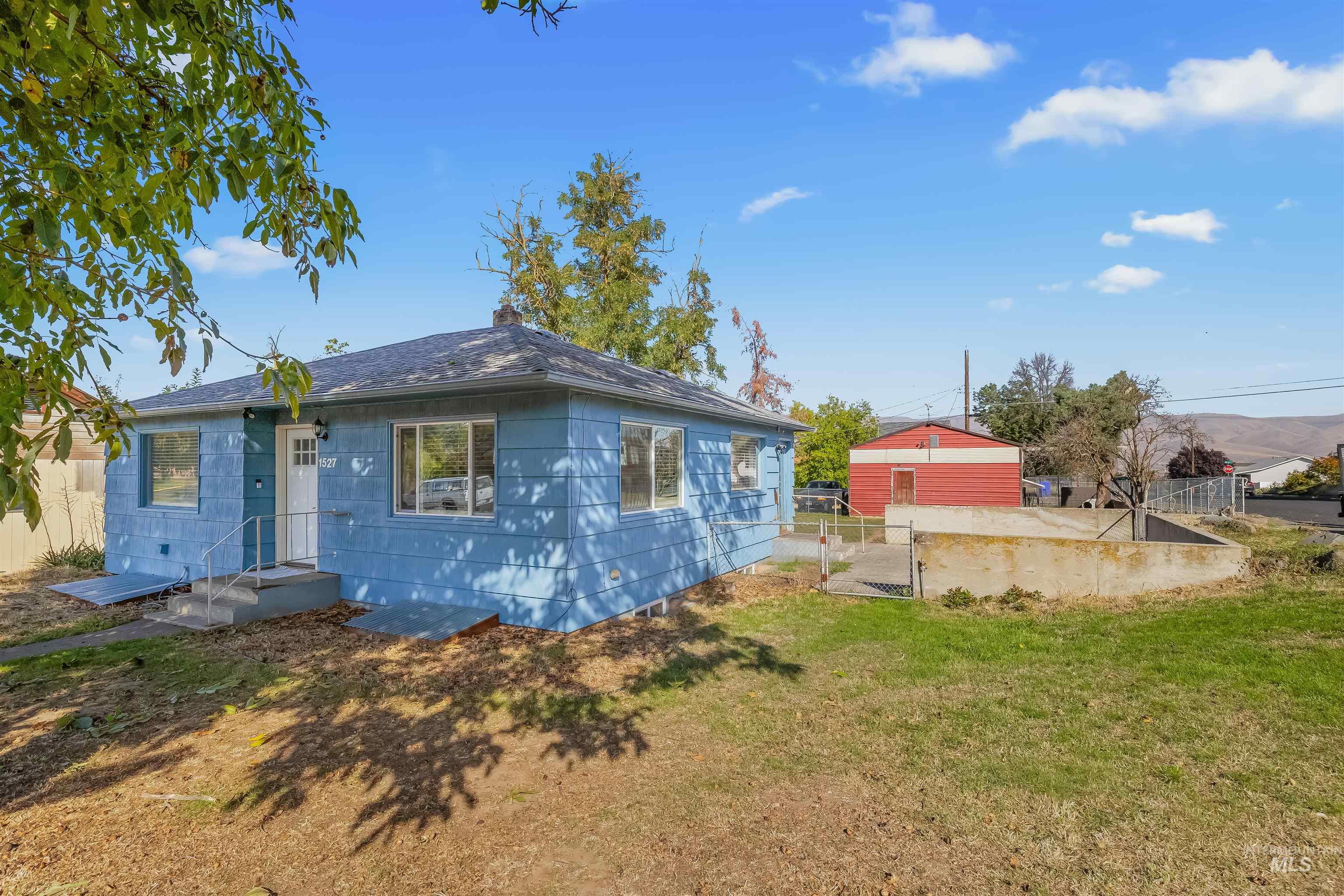 Blue single-story house with front steps and a fenced yard.