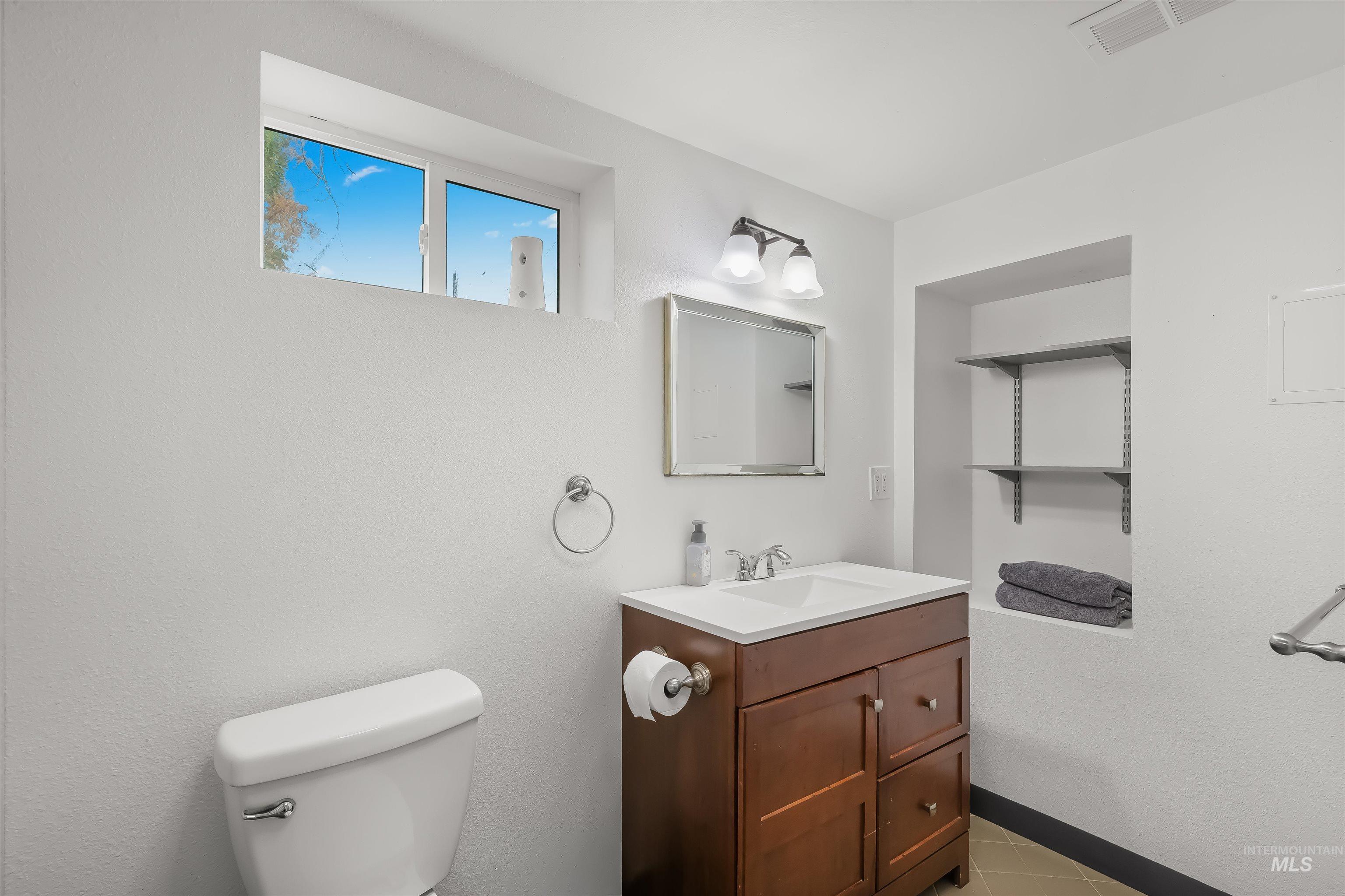 Bathroom with dark wood vanity, white sink, toilet, and recessed shelves holding folded towels.
