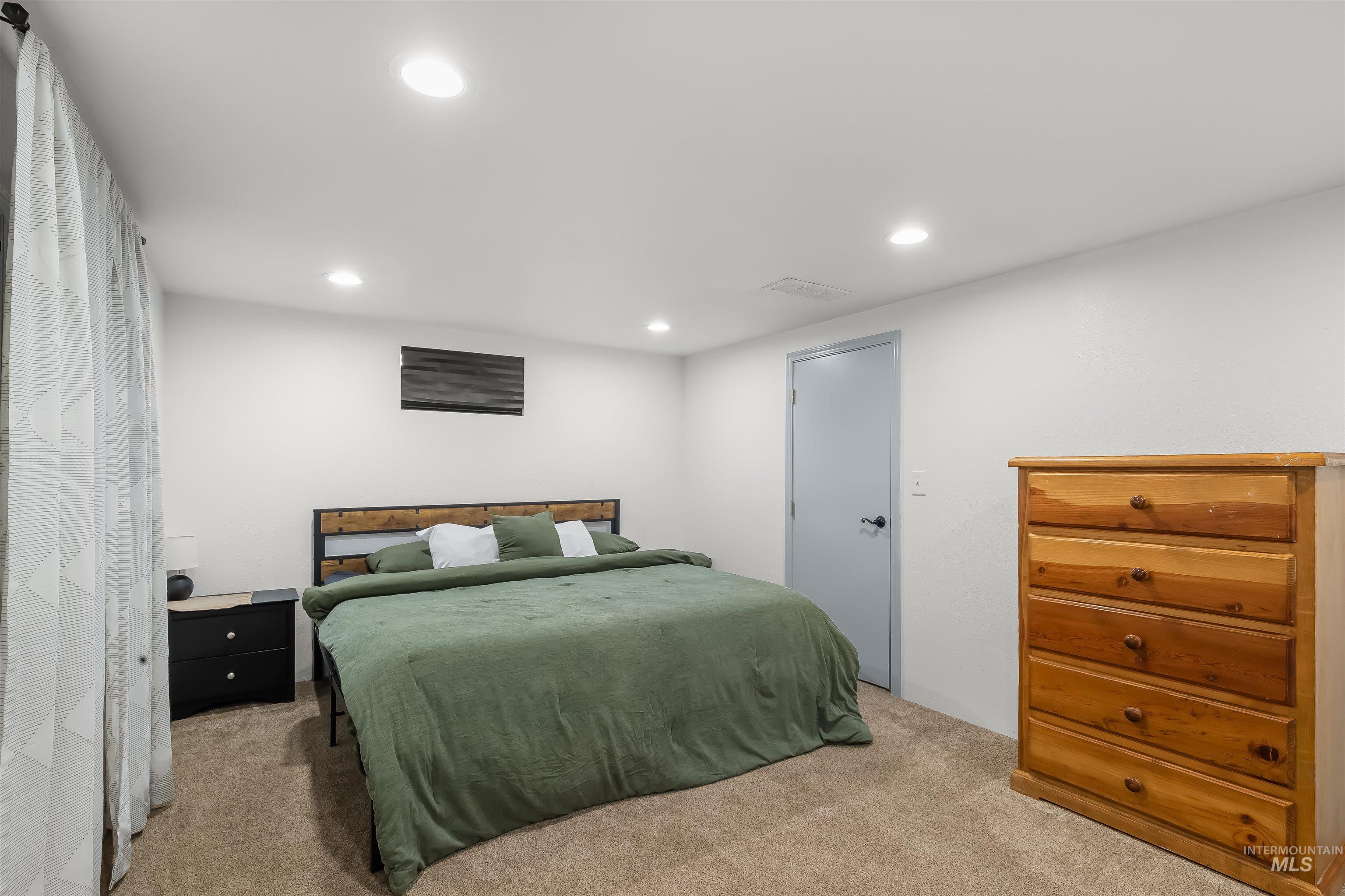 Bedroom with green bedding, a wood-and-black headboard, patterned curtains, and a wooden dresser.