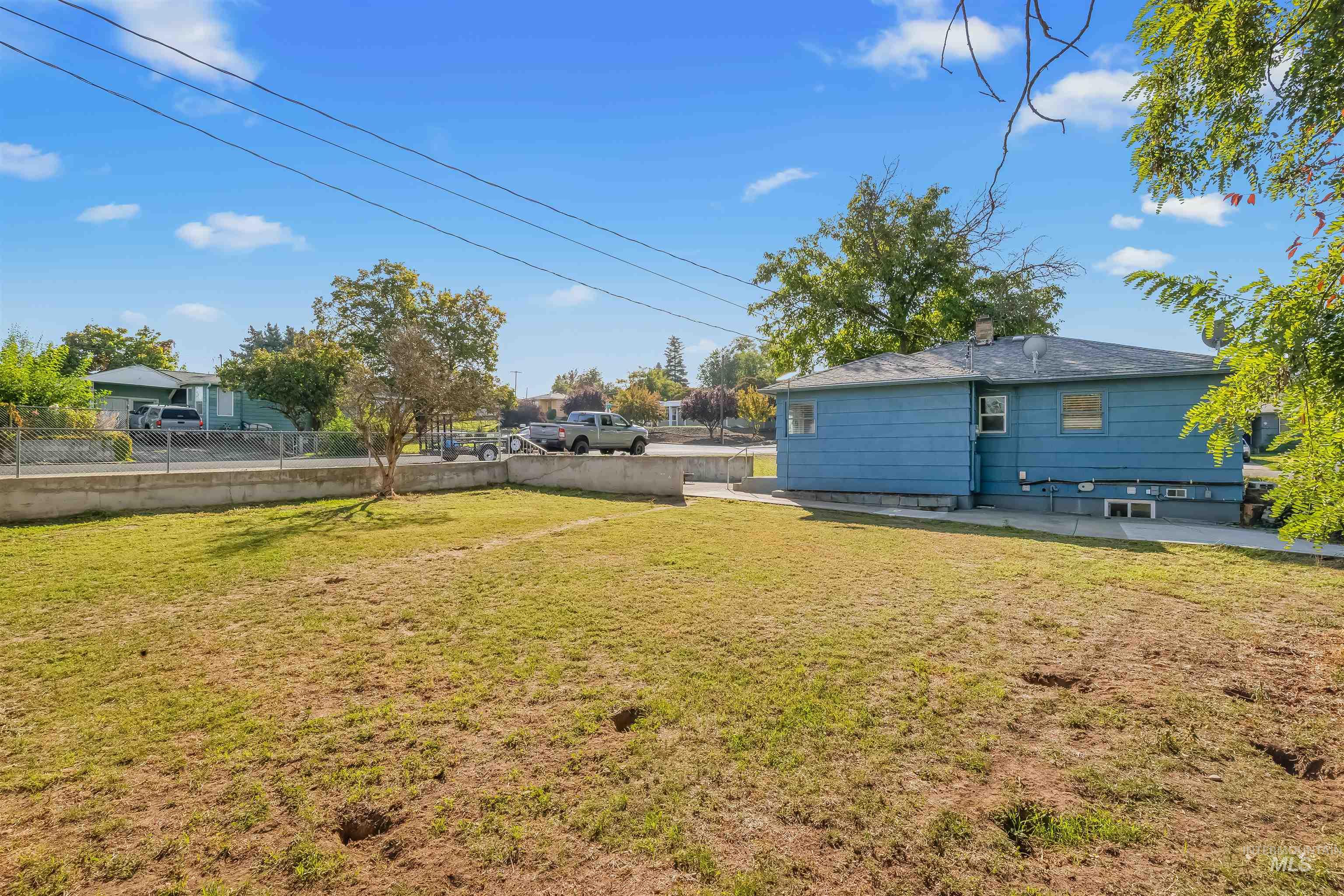 Blue house and dry grassy backyard bordered by a concrete wall and chain-link fence.