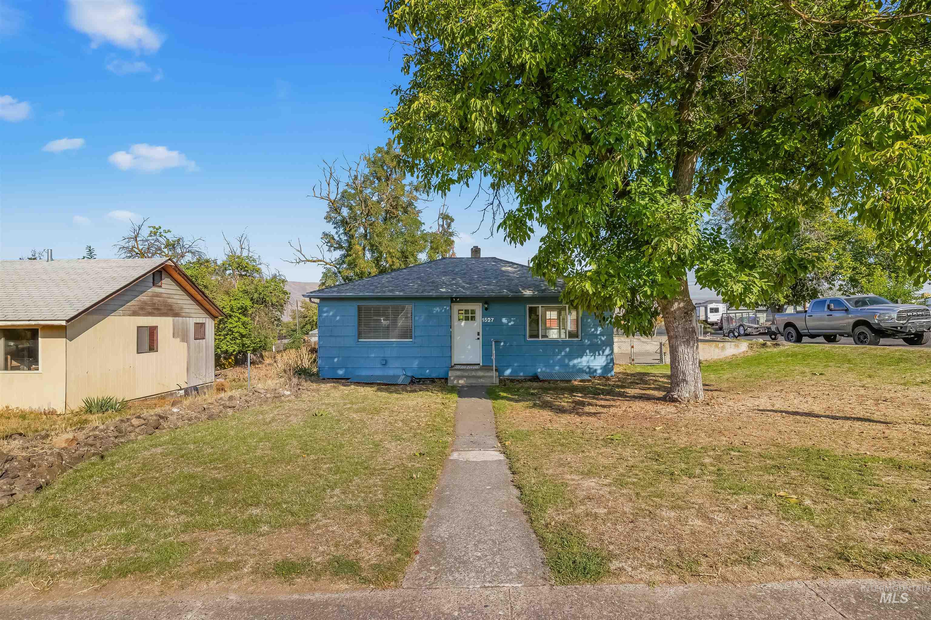 Blue single-story house with a large shade tree and a walkway to the front door.