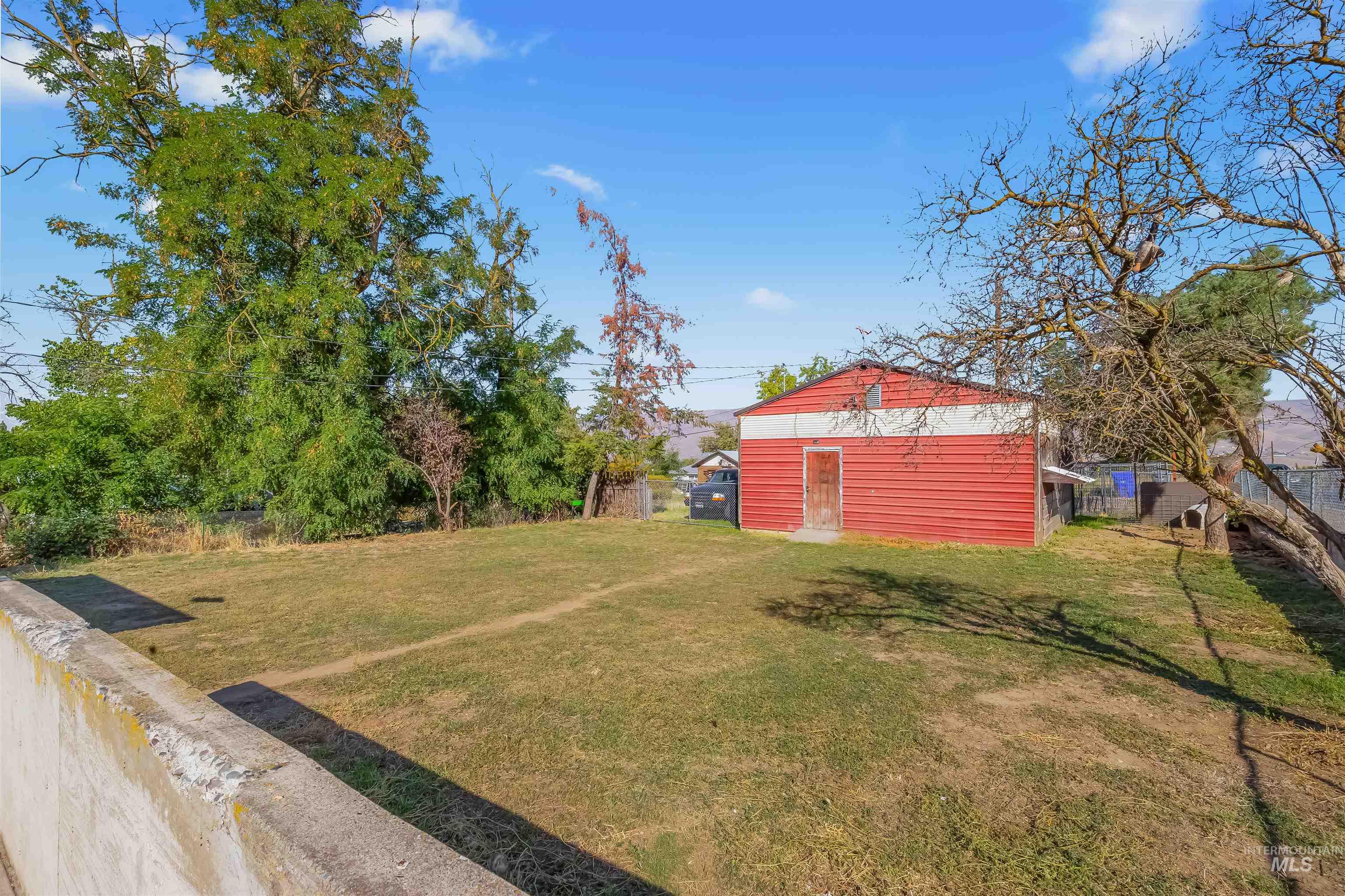 Grassy yard with a red detached outbuilding, mature trees, and a low concrete wall.