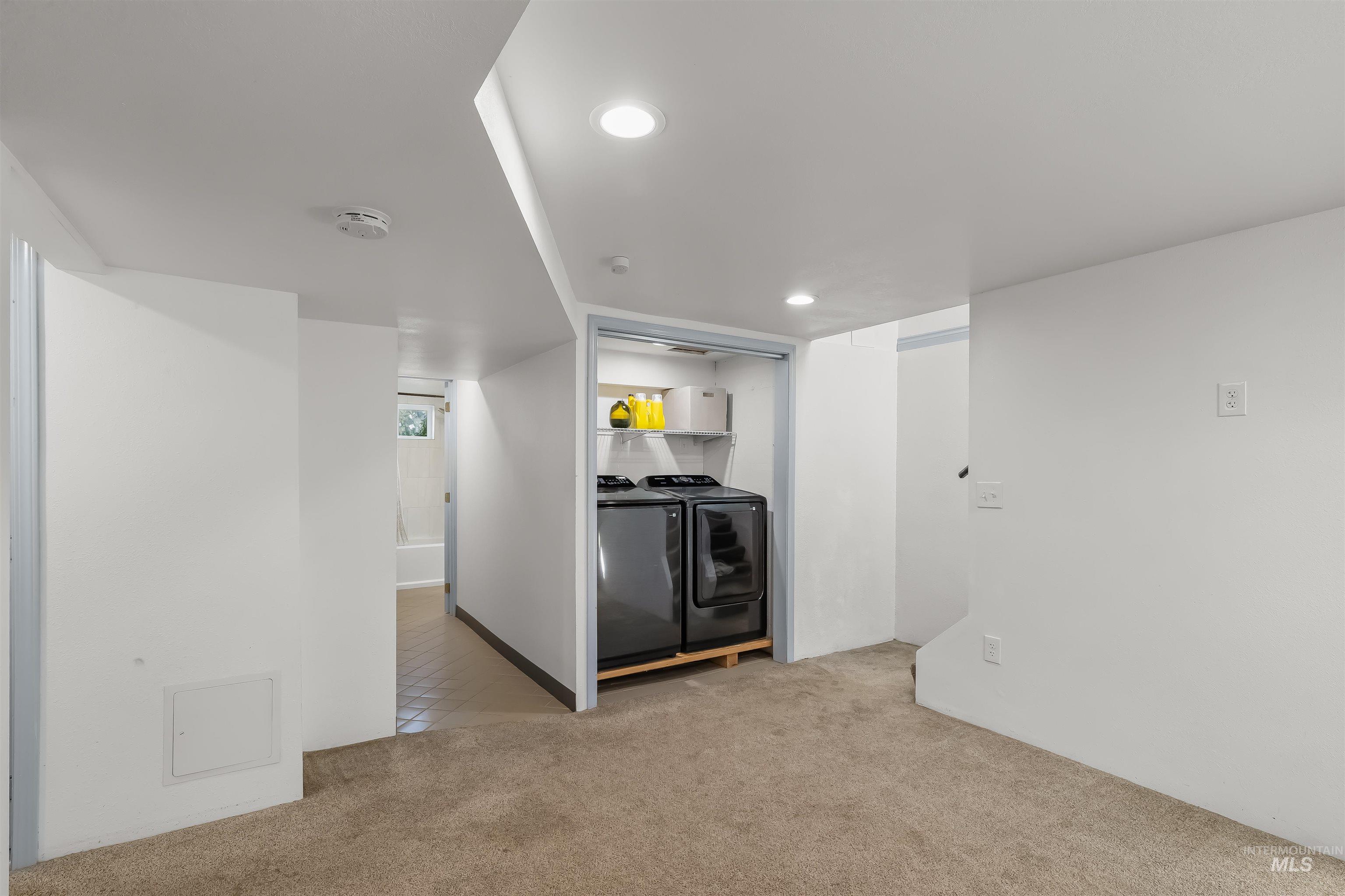 Carpeted room with a recessed laundry area and side-by-side washer and dryer.