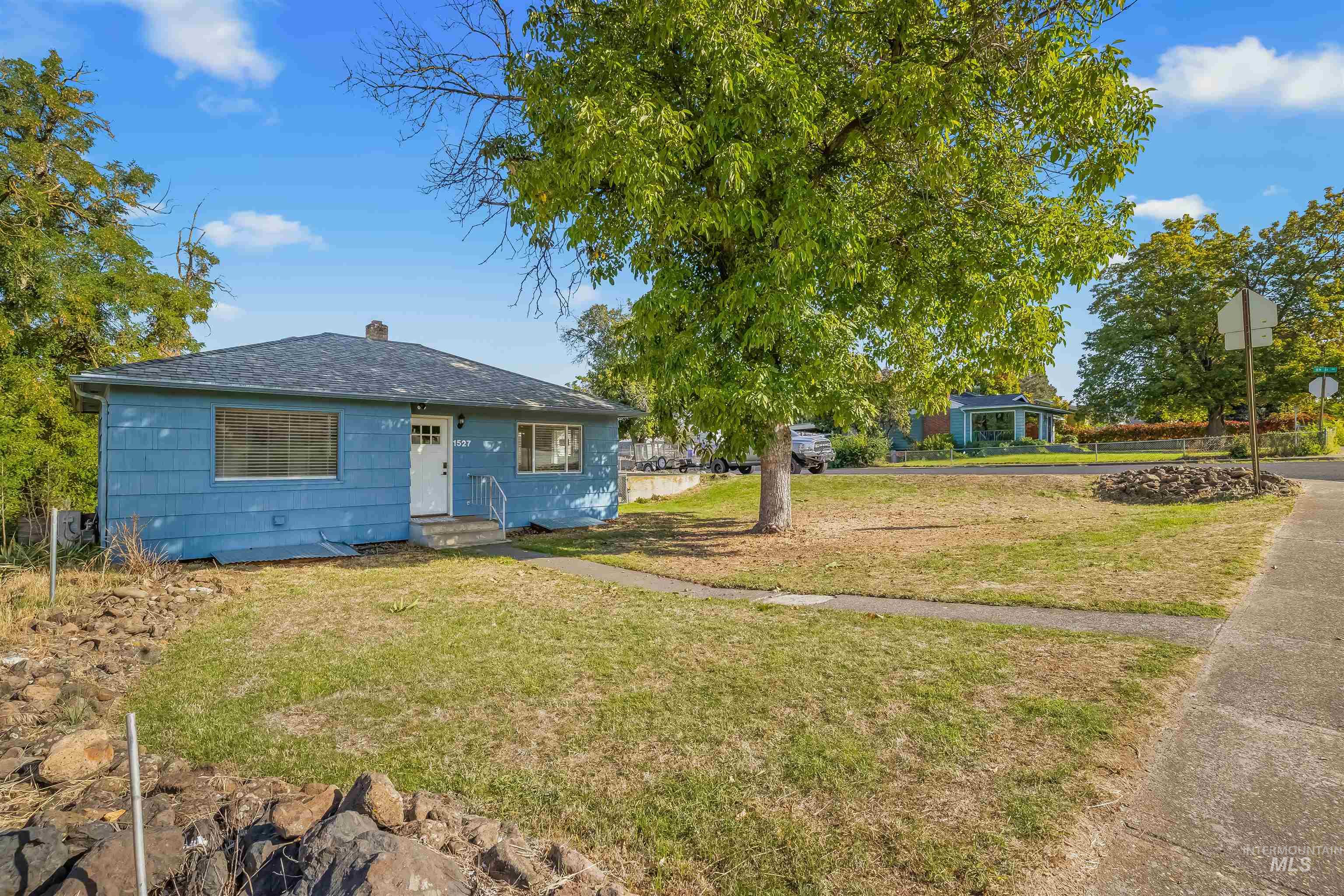 Blue single-story house with a large shade tree in the front yard.