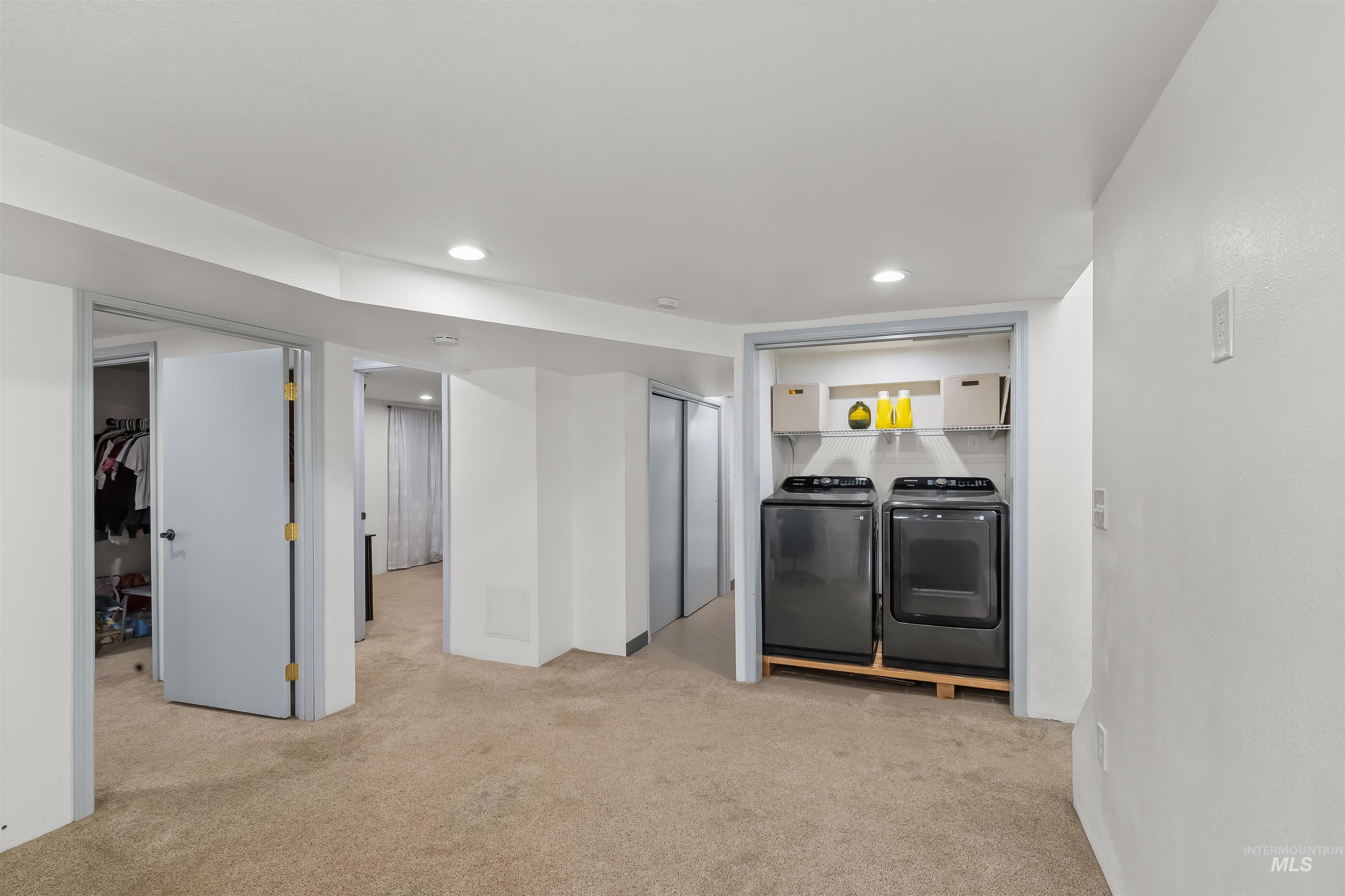 Laundry area with a dark washer and dryer beneath a wire shelf, beside carpeted rooms and open closets.