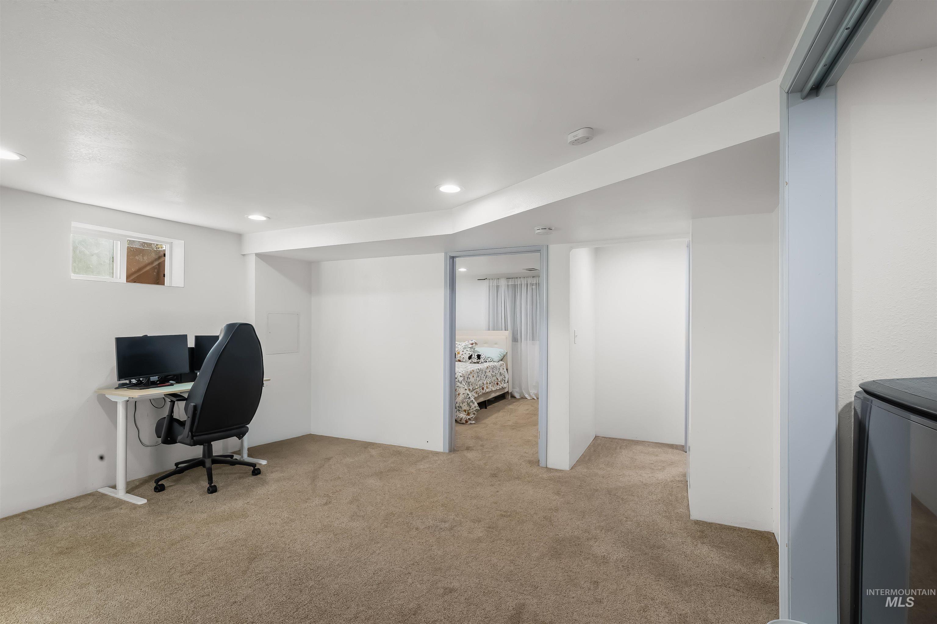 Finished basement workspace with a desk and monitors, opening onto a bedroom.