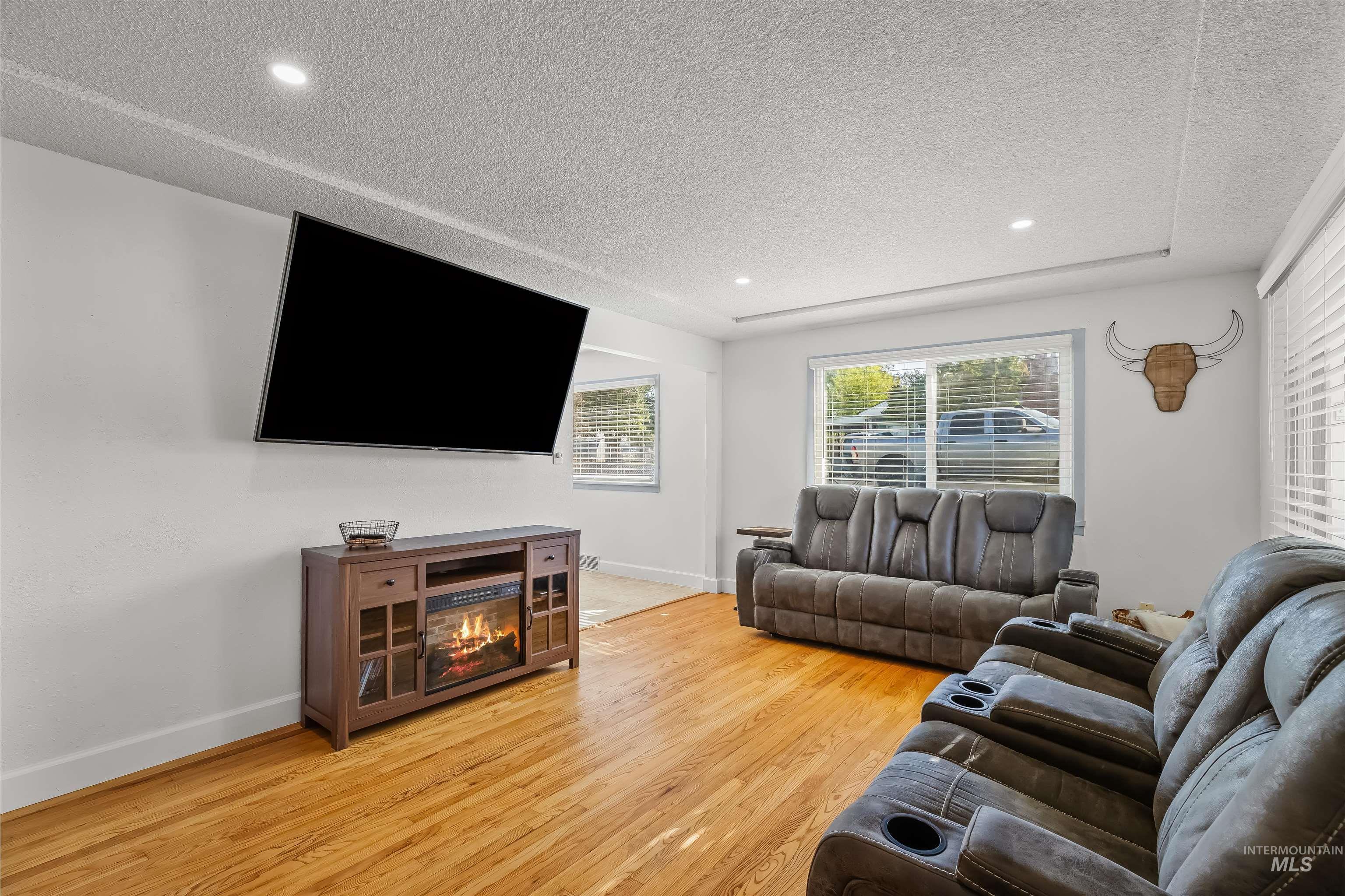 Living room with hardwood floors, gray reclining sofas, and a media console with an electric fireplace.